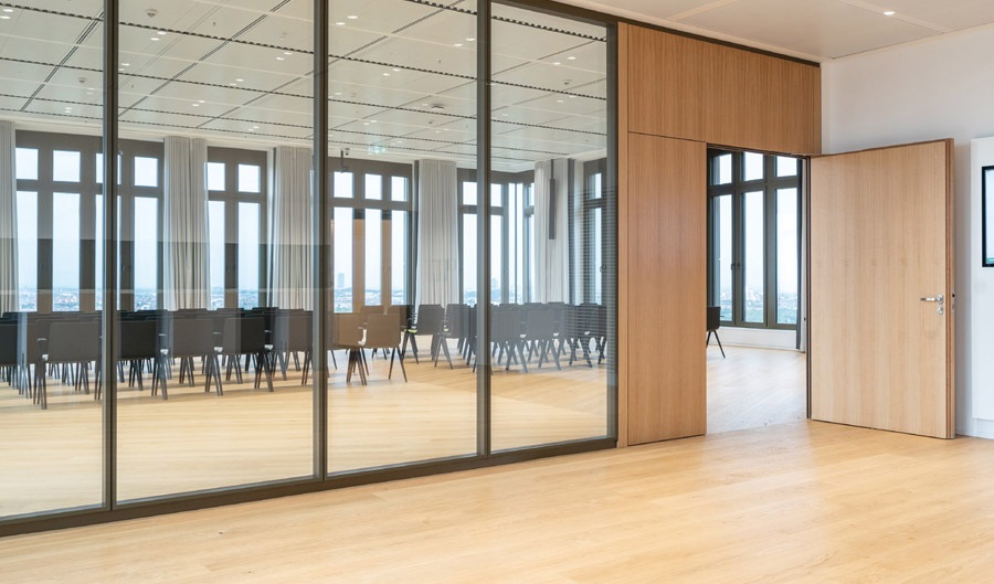 Blick durch eine Glaswand mit Holzboden auf schwarze Stühle